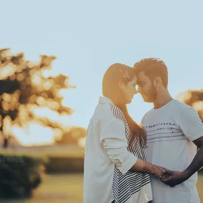 A quiet moment as the sun sets. This golden hour engagement photo uses the soft backlight to create a beautiful silhouette effect, highlighting the couple's connection as they hold hands and touch foreheads.