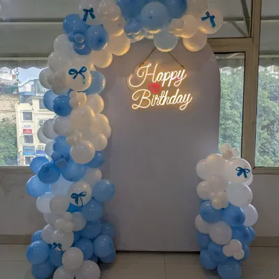 A beautiful balloon arch in pastel blue and white with a neon "Happy Birthday" sign, creating an elegant photo point or entrance for a party.