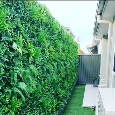 A dense, jungle-style vertical garden installed along a narrow walkway. This design uses a variety of artificial ferns and leafy plants to create a rich, textured look that provides privacy and greenery.