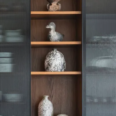 There’s a quiet poetry to rustic vases. Here, a collection of them is displayed in a fluted glass cabinet, their raw, weathered finish bringing depth and character to the polished space.