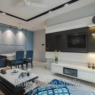 This wide view shows how the living and dining areas connect in an open-plan layout. The consistent color scheme of blues and whites, along with the marble-finish flooring and track lighting, creates a unified and spacious feel throughout the entire zone.