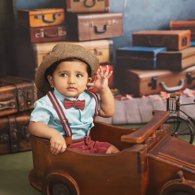 Waving goodbye to the baby days. This little traveler, complete with a hat and bowtie, is ready for his next big adventure in this vintage-themed studio shoot.