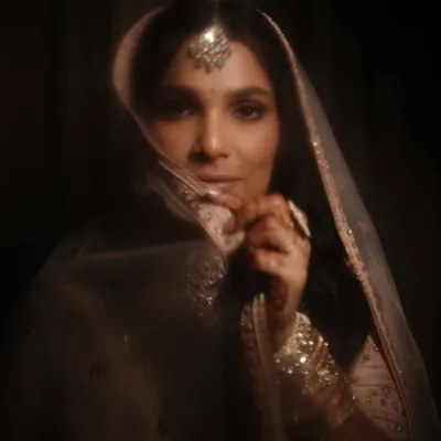 This is the epitome of timeless bridal elegance. Set against a dark, moody backdrop, her soft golden eye makeup and luminous skin create a dreamy, ethereal effect. Her hair is styled in a classic half-down look, perfect for her pastel pink lehenga.