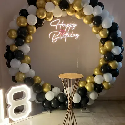 A classic black, white, and gold ring setup for an 18th birthday, complete with a neon sign, marquee numbers, and a cake stand.