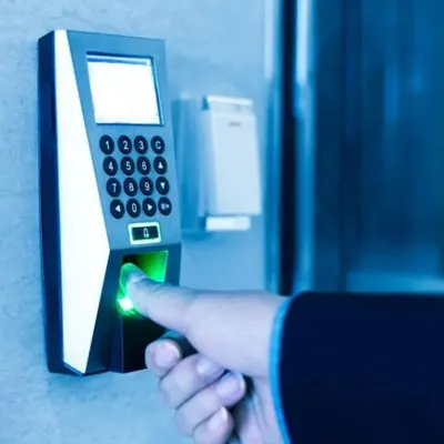 A user authenticating with a wall-mounted biometric fingerprint scanner. We install these advanced access control systems to provide secure, keyless entry for commercial buildings and offices.