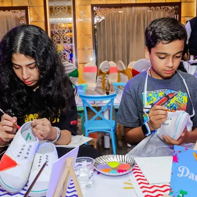Kids deeply focused on painting their own canvas shoes. This DIY activity is a fantastic way for them to express their creativity and take home a unique, wearable souvenir.
