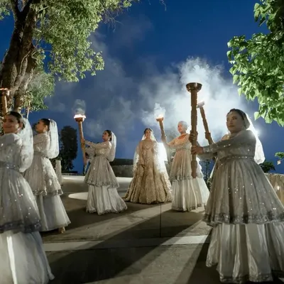 A dramatic and opulent bridal entry. The bride is flanked by women holding torches, creating a path of light for her. This is cinematic storytelling, making a wedding moment feel like a scene from a historical epic.