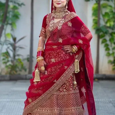 A full-length portrait of a bride in a stunning red embroidered lehenga, showcasing the classic North Indian bridal look.