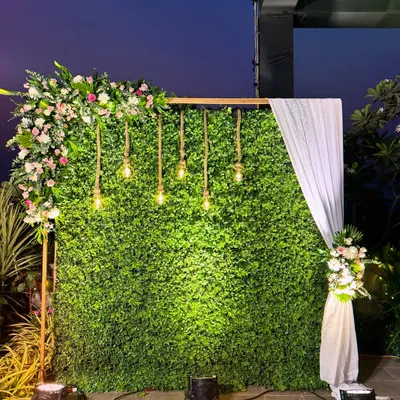 A modern and chic photo backdrop featuring a lush greenery wall. I added an asymmetrical floral arrangement, hanging Edison bulbs, and a simple white drape for a stylish and versatile photo corner.