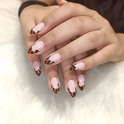 A classic French with a wild twist. This design features a traditional nude base on almond-shaped nails, but the tips are finished with a hand-painted leopard print for a fun and fierce look.