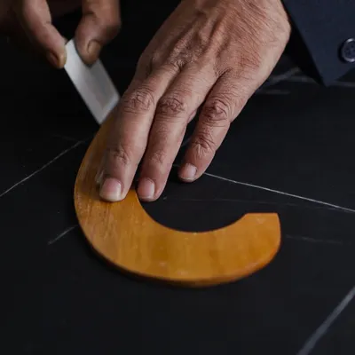 The first mark of a master craftsman. Here, our bespoke cutter uses traditional tools to chalk the pattern directly onto the fabric. This foundational step requires immense precision and an expert eye, as it dictates the final form of the garment.