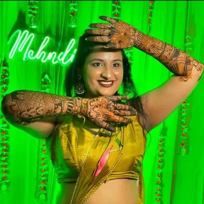 A happy bride posing with her full bridal mehendi against a festive green backdrop. Her joy and beautiful henna are what make my work so rewarding.