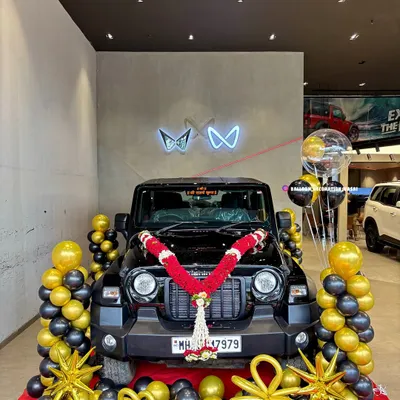 A stunning black and gold balloon setup for a new Mahindra Thar delivery. The display includes balloon pillars, star-shaped foil balloons, and a traditional red and white flower garland to make the vehicle handover ceremony truly memorable.