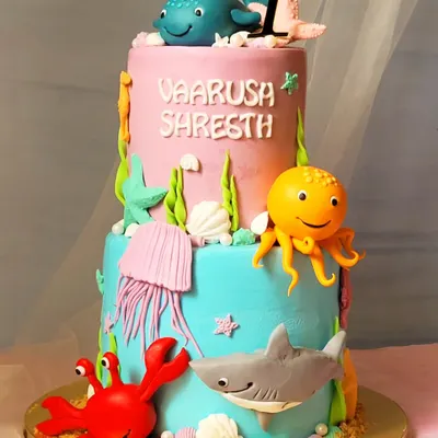 A vibrant two-tier "Under the Sea" themed cake. This one features a friendly shark, octopus, crab, and whale, all handcrafted to create a fun underwater adventure.