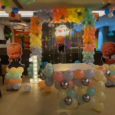 A Boss Baby theme for a first birthday party. This setup includes a colorful balloon arch, character cutouts, and a large light-up number '1' to mark the special occasion.