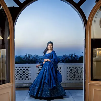 A beautiful engagement portrait of a bride-to-be in a stunning blue lehenga. She is framed by an elegant archway, creating a grand and picturesque scene to celebrate her special day.