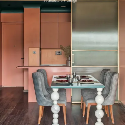 The dining area in Project 704 is a showcase of custom design and bold color. The table features a simple glass top on legs made of individually stacked marble spheres, set against a warm terracotta wall.