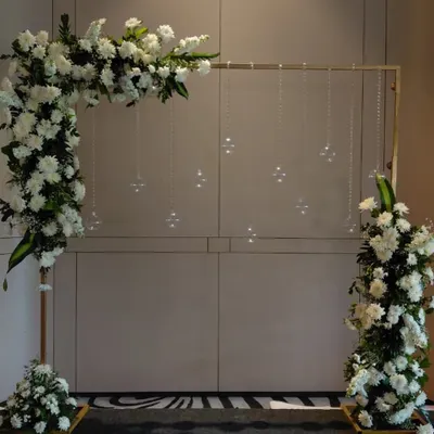 A minimalist and modern floral frame for a Bou-Bhaat or reception event. The asymmetrical arrangement of white flowers and hanging crystals creates a chic and elegant photo corner.