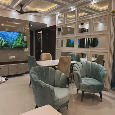 A bright and airy living and dining area featuring our custom-designed, shell-backed accent chairs in a soft sea-green velvet. The space is tied together with a modern dining set and a mirrored wall panel that enhances the room's spaciousness.