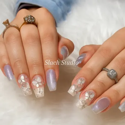 This elegant set on coffin extensions features a combination of shimmery lilac polish and nails with 3D sculpted white flowers and rhinestone details. It's a perfect example of detailed bridal or special occasion nail art.