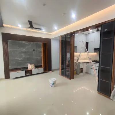 A nearly completed living area, showing the integration of the TV unit and the open kitchen entrance. The design focuses on clean lines and a harmonious flow between spaces.