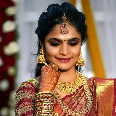 A detailed portrait of a bride's reception makeup. The look features classic gold jewelry, a neat hair updo with a maang tikka, and eye makeup that makes her features pop for the camera.