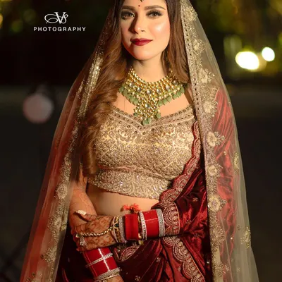 A stunning full-length portrait of a bride in her magnificent red and gold wedding lehenga. Her confident pose and direct gaze capture the essence of a modern, royal bride.