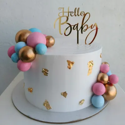 An elegant baby shower cake with pink, blue, and gold decorative balls and gold leaf accents. A beautiful way to say "Hello Baby."
