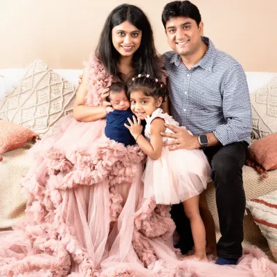 A beautiful family of four portrait, with mom in a stunning pink gown holding her newborn son while dad and big sister gather close.