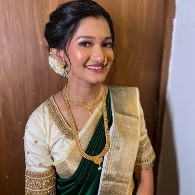 A classic engagement look. The bride is glowing in a dark green saree with a contrasting cream blouse. Her makeup is soft and dewy, and her hair is in a beautiful bun adorned with gajra.