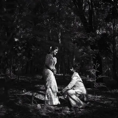 A dramatic, high-contrast black and white photo of a proposal in the forest. The monochrome edit emphasizes the light and shadow, creating a powerful and emotional scene.