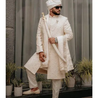 A portrait of pure regality. We designed this custom ivory sherwani for the groom who desires a look of classic, understated majesty on his wedding day, complete with a traditional turban and sword.