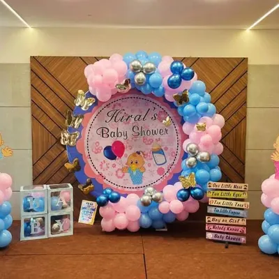 A classic baby shower setup with a 'Boy or Girl?' theme. The circular backdrop for 'Hiral's Baby Shower' is framed by pink and blue balloons, with cute baby cutouts on either side.