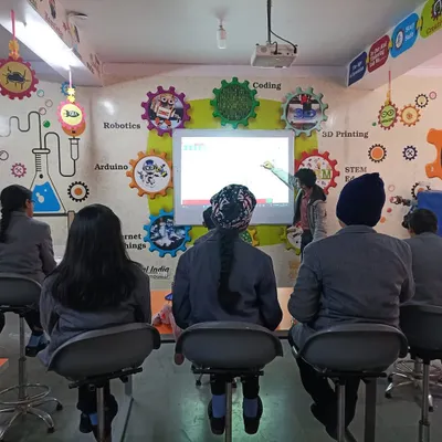 An instructor presents to a class in a fully equipped Atal Tinkering Lab we designed. The engaging wall art and modern equipment, including a projector screen, create a stimulating learning environment.