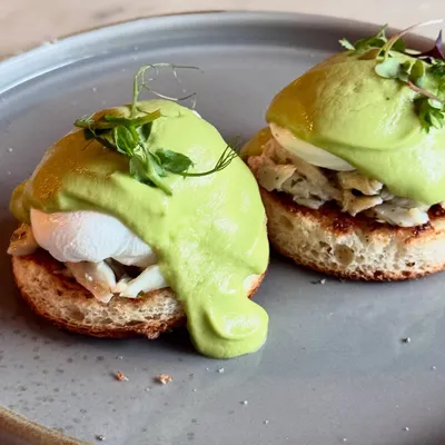 Our Crab Benedict, a signature dish on the Plats brunch menu. It features a generous portion of herb butter crab and a vibrant avocado hollandaise over perfectly poached eggs.