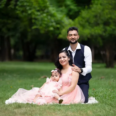 A classic family portrait taken in a lush green park. The family is dressed in coordinating pink and navy, sitting together for a beautiful outdoor photo.