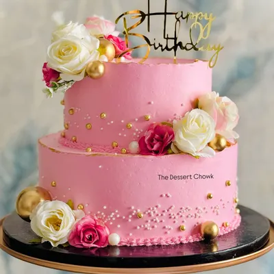 A beautiful two-tier custom birthday cake in a vibrant pink, decorated with white and pink roses and delicate gold pearls. This one was a pineapple flavor, perfect for a grand celebration.