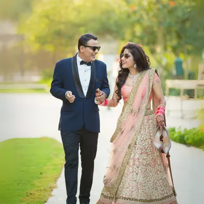 A fun, candid moment as the couple walks through a garden. The groom is dressed in a sharp tuxedo and the bride in a beautiful lehenga, showcasing a modern fusion look.