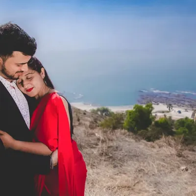 A tender embrace on a hillside overlooking the ocean. The woman's vibrant red dress stands out against the natural landscape, creating a passionate and romantic pre-wedding portrait.