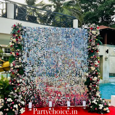 This shimmering silver sequin backdrop was created for a 75th birthday celebration. The wall is framed by columns of red and white flowers, creating a glamorous and celebratory photo spot by the pool.