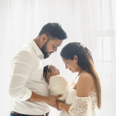 A tender portrait of new parents holding their swaddled newborn. The soft, directional light from the studio window creates a serene and intimate atmosphere, perfectly capturing the feeling of a new family.