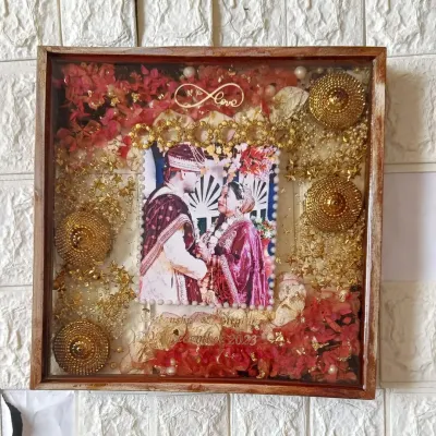 This square wedding keepsake frame is filled with vibrant red flowers and golden ornaments from the ceremony. The couple's photo is centered, surrounded by memories of their special day, including an infinity love symbol.