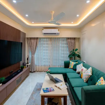 This modern living room features a striking emerald green L-shaped sofa. We balanced the bold color with a neutral palette, a fluted wooden panel for the TV unit, and warm cove lighting for a sophisticated feel.