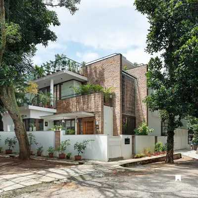 The exterior of the Twin Courtyard House, nestled among lush trees in Bangalore. The facade uses natural stone cladding and large openings to hint at the light-filled, nature-integrated spaces within.