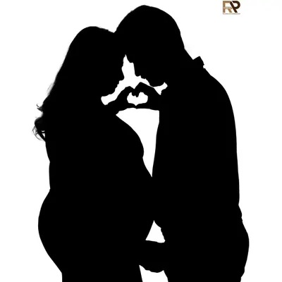 A beautiful silhouette of an expecting couple forming a heart with their hands over the baby bump. This artistic shot uses shadow and light to create a powerful symbol of love.