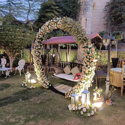 A beautiful garden setup perfect for an evening engagement or sangeet. The floral swing is the centerpiece, surrounded by lanterns and soft lighting to create a magical atmosphere.