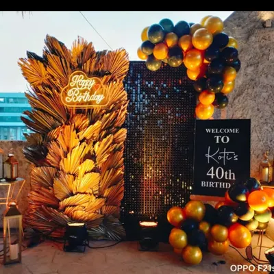 A sophisticated 40th birthday photo booth. The decor features a black sequin wall, a large arrangement of dried golden palm leaves, and a custom neon sign.