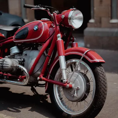 A detailed close-up of the front wheel and engine of a vintage red BMW motorcycle. This shot highlights the classic design and mechanical beauty of the bike, focusing on its historical craftsmanship.