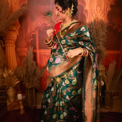 A stunning solo portrait of a mother-to-be in a traditional green and gold floral saree. The rich fabric and intricate details are highlighted against a warm, ornate backdrop.