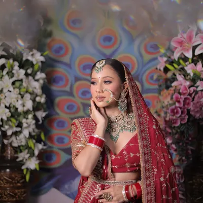 A mid-shot of the bride in a red embroidered lehenga, set against a floral and peacock-themed backdrop.